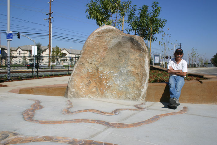 The artist Sam Tubiolo sits next to one of the large entrance boulders at Hazel Light Rail station in Rancho Cordova.